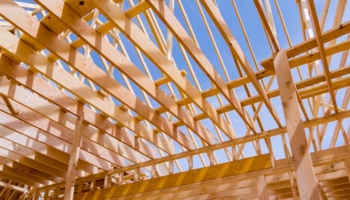 Das Holzgerüst eines im Bau befindlichen Hauses mit freiliegenden Balken und Dachstühlen - ein klassisches Beispiel für den modernen Holzbau - steht vor einem klaren blauen Himmel.